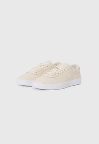Lys beige sneakers med en glatt semsket tekstur, hvit gummisåle og minimalistisk design, med snørebånd og en liten merkevarelogo.