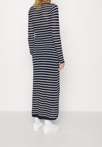 Dlouhé pletené šaty s vodorovnými námořnickými modrými a bílými pruhy. Kulatý výstřih, dlouhé rukávy a rovný silueta. Nosené s bílými teniskami.