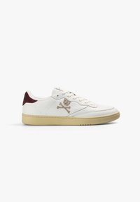 Zapatilla de cuero blanca con un logotipo de calavera y huesos en color beige. Los acentos en el talón son de color burdeos y la suela es de goma, lo que completa el diseño.
