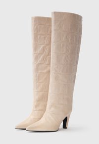 Stivali beige al ginocchio con texture coccodrillo, punta affusolata e tacco nero di 3 pollici. Superficie liscia e lucida con un design strutturato.