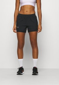 Pantalones cortos deportivos negros con cinturilla elástica. Combinados con un sujetador deportivo lila claro y zapatillas de running negras con detalles rojos.