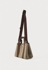 Μικρή μπεζ υφασμάτινη τσάντα με σκούρες καφέ κάθετες ρίγες, δύο κοντές λαβές και έναν μακρύ ρυθμιζόμενο ιμάντα ώμου, τοποθετημένη σε λευκό φόντο.