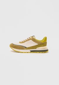 Sneaker met een combinatie van lichtbeige suede en olijfgroene accenten. Beschikt over een dikke witte tussenzool en een gele rubberen buitenzool.