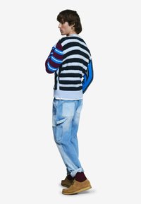 Pruhovaný sveter s mixom farieb vrátane čiernej, bielej a modrej, zosúladený s svetlomodrými džínami a hnedými topánkami. Textúrovaný pletený detail.