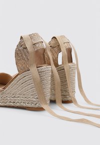 Alpargatas de cuña con parte superior de tela beige tejida, acentos dorados en contraste y largas cintas beige; tacón de yute trenzado texturizado.