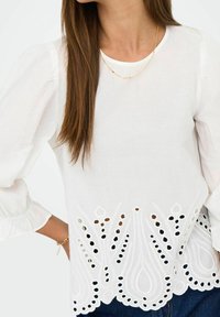 Weißes Blusenshirt mit langen, gepufften Ärmeln; verfügt über komplexe durchbrochene Stickerei am Saum, die Textur und Detail hinzufügt. Lässige Passform.