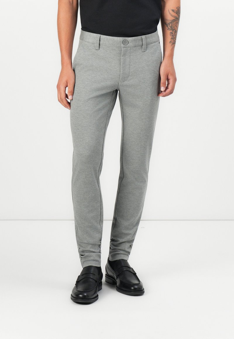 Pantalones ajustados de color gris claro, confeccionados en una tela suave, con cierre de botón, trabillas para cinturón y bolsillos laterales, combinados con mocasines negros.