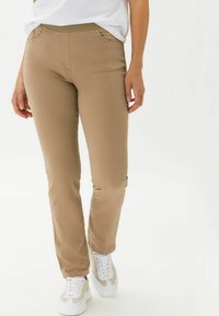 Pantalons ajustés beige avec une texture lisse, dotés de poches latérales et d'une ceinture élastique confortable. Portés avec des baskets blanches.