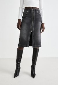 Gonna midi in denim nero con zip frontale, cinque tasche e vita aderente. Abbinata a stivali neri con tacco a spillo al ginocchio.