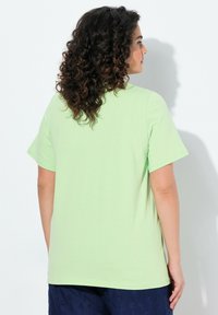 T-shirt a maniche corte, colletto tondo, in cotone verde chiaro, con una vestibilità comoda. Texture liscia, design semplice, senza motivi o accenti visibili.