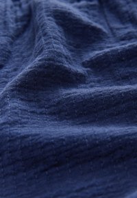 Marineblauwe textuurstof met een gekreukeld oppervlak. Heeft een subtiel ruitpatroon, gemaakt van zacht, geweven materiaal.