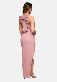 Robe maxi en tissu rose doux avec dos nu, grand détail de nœud, fente haute sur le côté droit et décolleté halter.