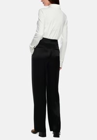 White long-sleeve shirt paired with high-waisted, black satin pants. Pants feature side pockets and a smooth texture with a tailored fit.