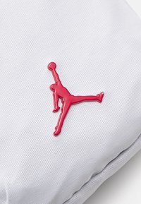 Red rubber Jordan logo on a textured white fabric background, featuring a jumping figure with a raised arm and ball.