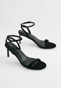Sandali con tacco in suede nero, dotati di sottili cinturini alla caviglia, design aperto sulla punta e interno liscio. Caratterizzati da un moderato tacco a stiletto.