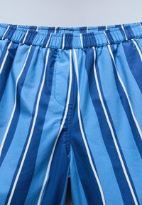 Μπλε παντελόνια με ελαστική μέση και κάθετες ρίγες σε διαφορετικές αποχρώσεις του μπλε και λεπτές λευκές γραμμές, απαλό ύφασμα και εμφανής ραφή στη φερμουάρ.