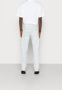 Jean délavé clair, coupe droite, cinq poches et surpiqûres contrastantes. Associé à un t-shirt blanc uni et des baskets noires.