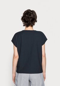 Tmavě modrý volný top s krátkými rukávy, texturovaná tkanina a kulatý výstřih; zadní pohled ukazuje rovný lem a uvolněný střih.