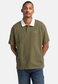 Olivgrön polo skjorta med vit krage, korta ärmar och en liten broderad logotyp på bröstet. Har en strukturerad tyg.