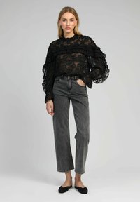 Blouse en dentelle noire avec un motif floral, manches volantes, associée à un jean en denim gris taille haute et des chaussures plates noires.