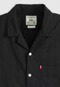Zwart kortemouwenshirt met geborduurde ovale patronen, twee witte knopen en een linkse borstzak met een rode Levi's label.