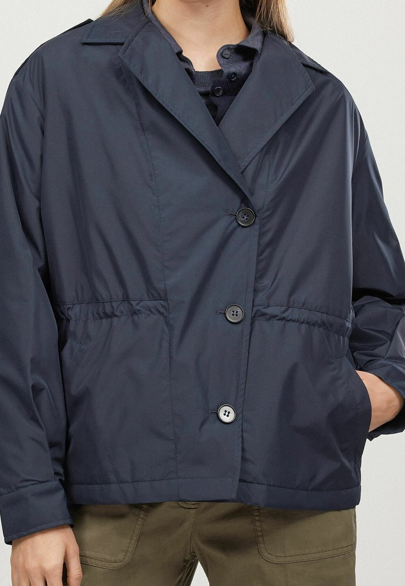 Mörkblå, lätt jacka med klassisk krage, framknäppning, elastisk midja och sidofickor; mjuk textur och avslappnad passform.