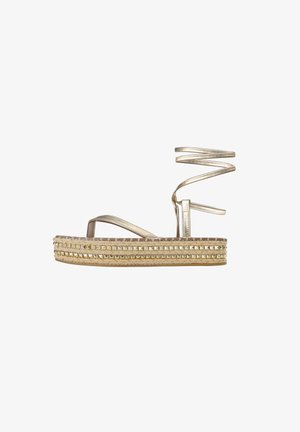 Goldene, metallische Plattform-Sandalen mit geflochtenem Jute und Nietenakzenten. Sie sind mit einem spiralförmigen Knöchelriemen und einer flachen Sohle für Unterstützung ausgestattet.