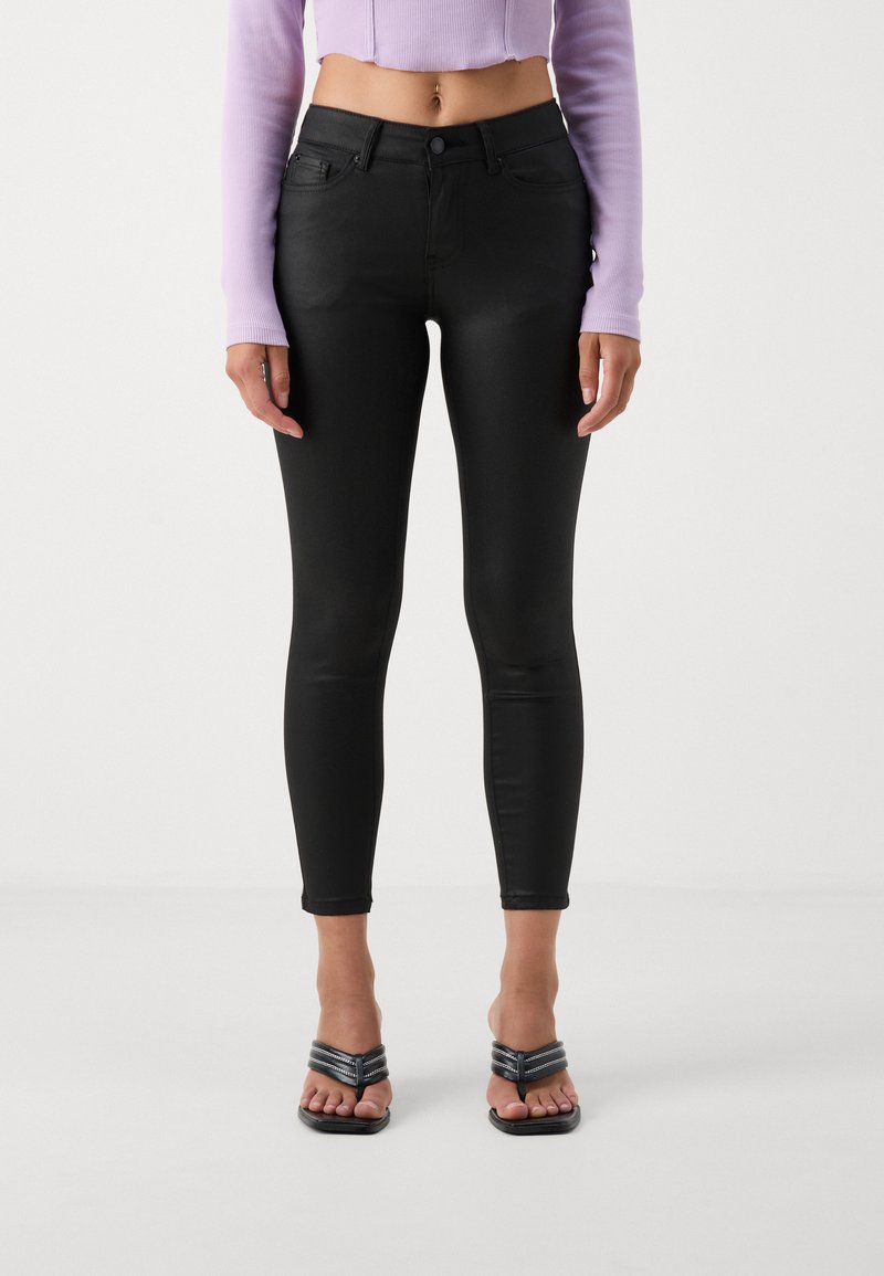 Zwarte skinny jeans van een gladde, rekbare stof. Hoog in de taille met voorzakken, gecombineerd met zwarte sleehakken.