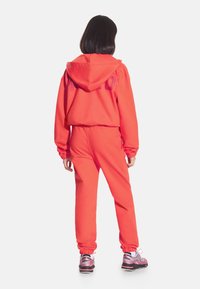 Czerwona bluza z kapturem i pasujące dresy wykonane z miękkiego materiału; posiadają elastyczne mankiety i pas; para butów sportowych dodaje kontrastu.