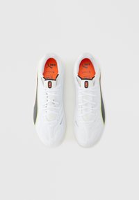 Białe buty sportowe o fakturowanej powierzchni, z czarnymi i neonowo-żółtymi akcentami, sznurowadłami oraz pomarańczowymi wkładkami z logo.