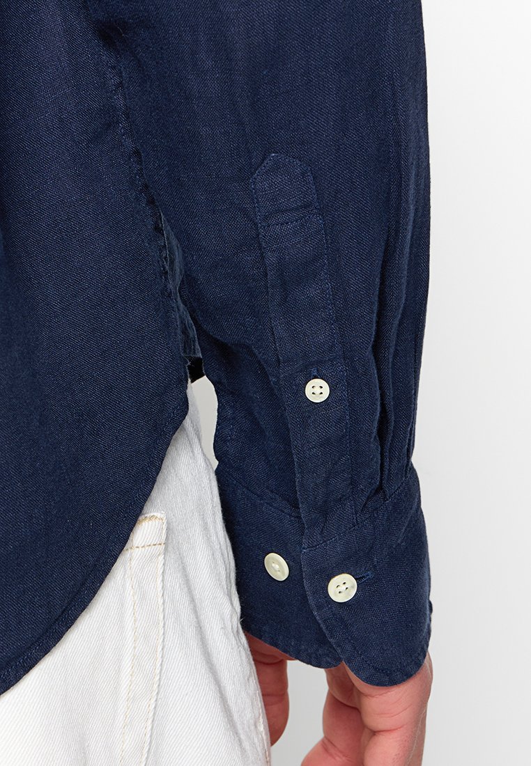 Camisa de lino azul marino con puño abotonado, con un acabado texturizado y un corte ajustado. El puño tiene dos botones redondos de color crema.