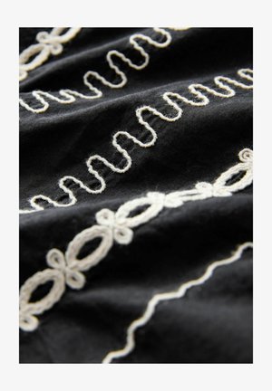 Czarna tkanina z białymi haftowanymi wzorami, w tym falistymi liniami i owalnymi kształtami, o teksturowanej powierzchni i misternych detalach.