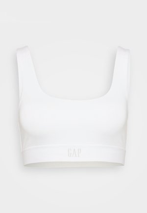 Weißer nahtloser Sport-BH mit breiten Trägern und GAP-Logo auf dem elastischen Band, präsentiert vor einem hellgrauen Hintergrund.