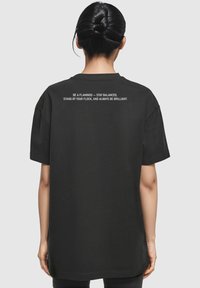 T-shirt in cotone nero con maniche corte e vestibilità comoda, con testo bianco stampato sul retro che riporta un messaggio motivazionale.