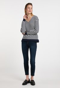 Pulover raiat în dungi albastre și albe, cu decolteu în V, manșete și tiv cu model în relief; asortat cu blugi skinny negri și mocasini negri.