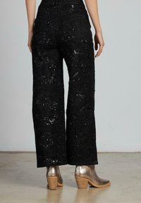 Pantaloni neri a gamba larga con design floreale ricamato e paillettes. Abbinati a stivali metallici alla caviglia con tacco impilato.
