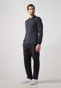 Fekete, hosszú ujjú póló függőleges fehér csíkokkal, slim-fit. Fekete nadrággal és fehér sportcipővel párosítva, minimális dizájnnal.