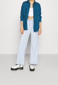 Camisa a cuadros azul, top corto blanco, pantalones de pierna ancha de un azul claro y zapatos de plataforma negros. Incluye una camisa con botones y una cintura con cordón.