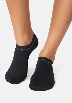 Schwarze Knöchelsocken mit glatter Textur und einer wellenförmigen grauen Nähte entlang des oberen Randes. Entworfen, um unter dem Knöchel zu sitzen.