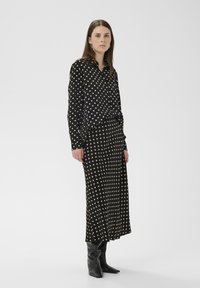 Ensemble blouse et jupe à pois noirs avec des points crème,dotée d'une coupe décontractée et de manches longues, associée à des bottes noires montant jusqu'aux genoux.