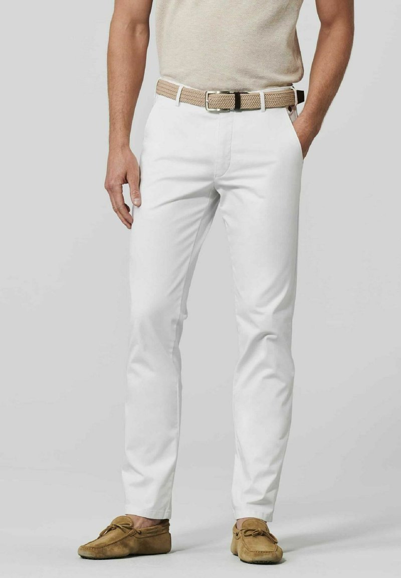 Chinos blancs en coton avec une coupe ajustée, arborant une ceinture tissée beige et des mocassins marron en cuir souple. La tenue est complétée par un haut beige clair.