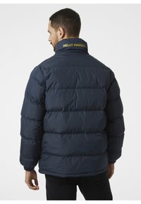 Granatowa kurtka puchowa z wysokim kołnierzem, cechująca się wyraźnymi szwami, miękką teksturą oraz żółtym logo "HELly HANSEN" na kołnierzu.
