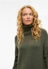 Pull à col roulé vert olive en tissu tricot texturé avec une coupe ample, doté d'un col à côtes haut et de manches longues.