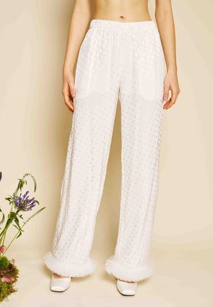 Białe przezroczyste spodnie w grochy z elastycznym pasem i falbankami u dołu, noszone przez stojącą osobę, w połączeniu z białymi, spiczastymi butami.