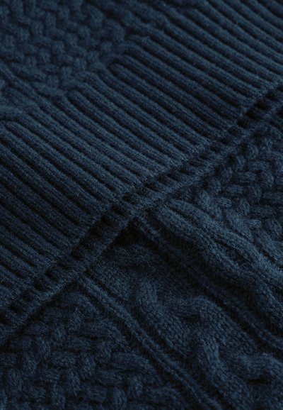Tengerés kék kötött anyag, texturált mintákkal, bordás részekkel és zsinórmintával. Puha tapintás, meleg megjelenéssel.