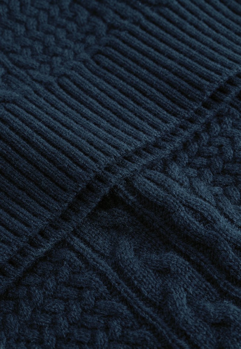 Tissu tricoté bleu marine avec des motifs texturés, présentant des sections côtelées et un design en tricot torsadé. Texture douce avec une apparence chaude.