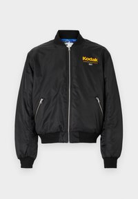 Giacca bomber nera con zip frontale, polsini e orlo a costine. Presenta un logo Kodak giallo sul petto e due tasche laterali con zip.