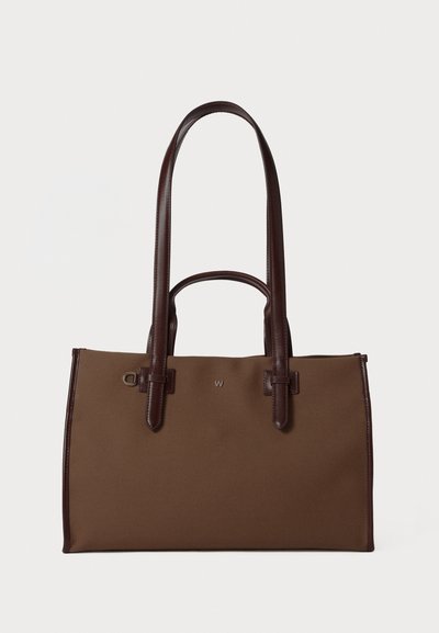 Sac fourre-tout en toile marron avec des poignées en cuir marron foncé. Présente une surface texturée subtile et un design minimaliste avec un accent logo.
