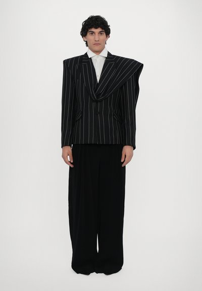 Black pinstriped double-breasted blazer with an asymmetric lapel, paired with wide-legged black trousers. Smooth fabric texture.