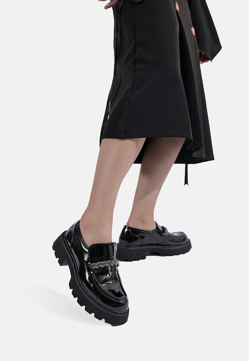 Scarpe nere in pelle verniciata con una larga cinghia e dettagli in argento, dotate di una suola nera spessa e una punta rotonda.